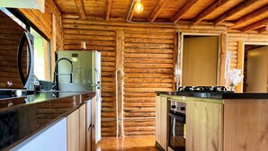 A log cabin kitchen with wooden walls, a central island, a refrigerator, a stove, and a sink.