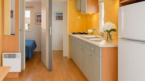 Cocina compacta con estufa integrada, un lavamanos y refrigerador. Cuenta con un pequeño comedor con mesa y sillas.