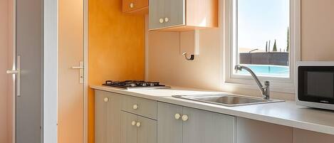 A compact kitchen with grey cabinets, a wooden accent wall, a window with a view, and a black trash bin.