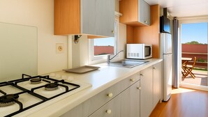 Una cocina moderna con estufa a gas, microondas y refrigerador, armarios de madera y ventana con vista a un patio.