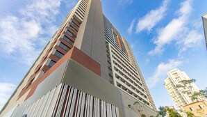 Un edificio de gran altura con diseño arquitectónico moderno, que destaca por un elemento vertical prominente y una serie de balcones.