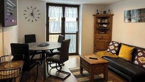 Un salon moderne comprenant un coin repas, un canapé, un meuble en bois et une grande fenêtre avec des rideaux.