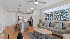 Eine moderne Küche mit einer zentralen Kochinsel, ein Essbereich mit Holztisch und ein Wohnzimmer mit Sofa und abstrakten Kunstwerken an der Wand.