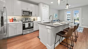 A modern kitchen with white cabinets, stainless steel appliances, and a central island with bar stools. - Luxury King 1bd Pool + Gym + Parking + Stockyards (Fort Worth)