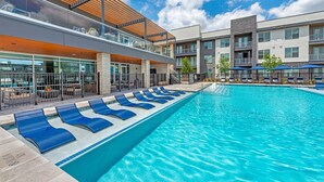 A swimming pool with lounge chairs, a covered seating area, and a modern building with balconies. - Luxury King 1bd Pool + Gym + Parking + Stockyards (Fort Worth)