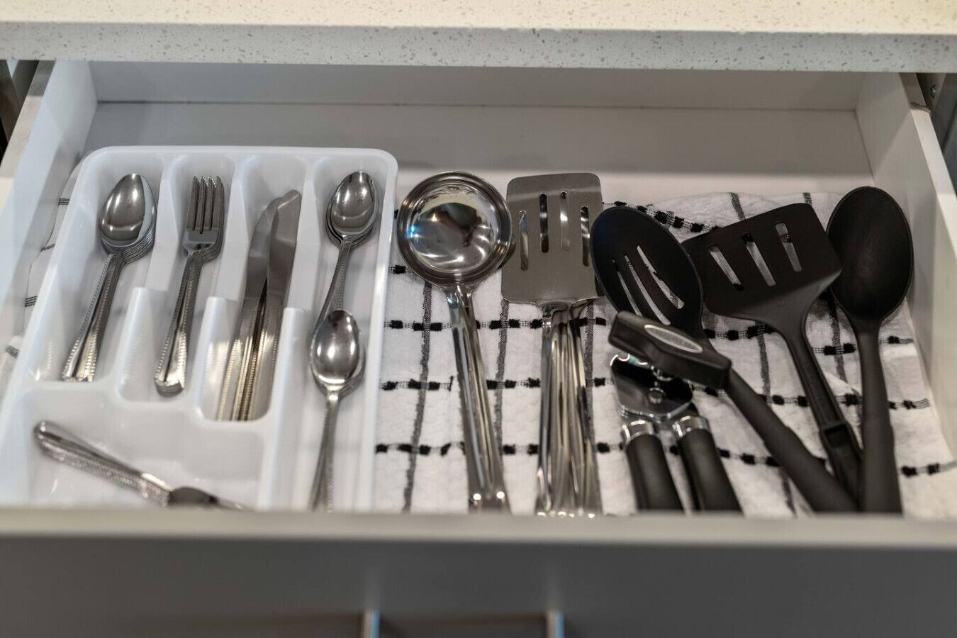 A drawer containing various kitchen utensils including spoons, forks, a spatula, and a ladle.