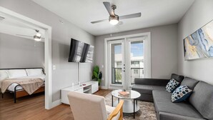 Een moderne woonkamer met een grijze bank, een salontafel, een televisie en een plafondventilator.