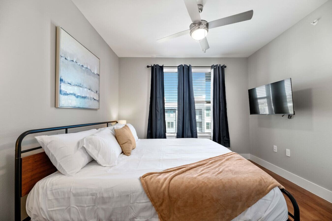 Ein Schlafzimmer mit Bett, Deckenventilator, Fernseher und einem Fenster mit Vorhängen.