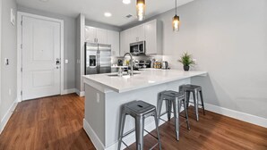 A modern kitchen with a large island, stainless steel appliances, and bar stools. - Stylish Luxury King Bed | Gym+Pool+Stockyards (Fort Worth)