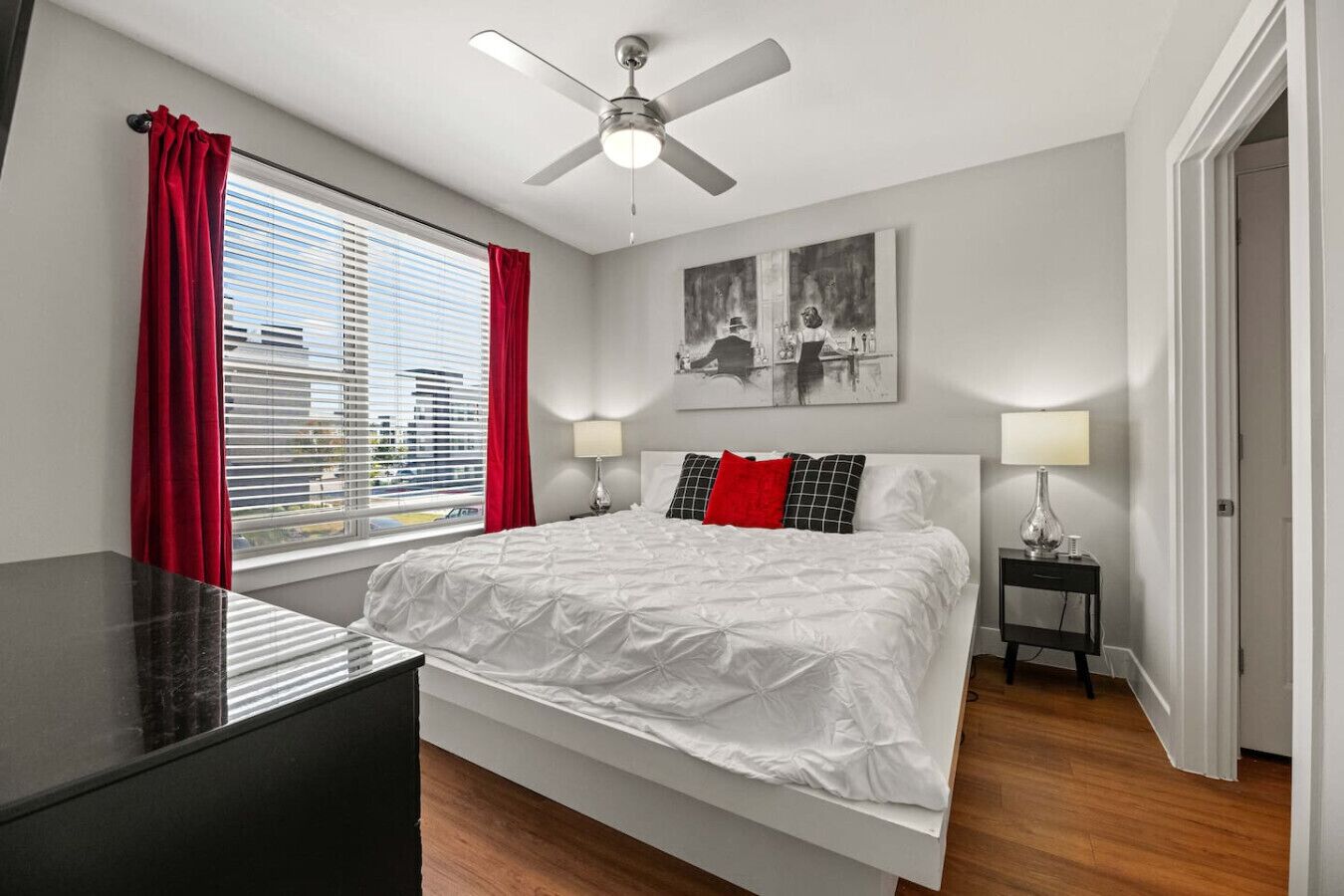 Une chambre moderne avec un lit, deux tables de chevet, un ventilateur de plafond et une fenêtre avec des rideaux rouges.