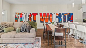 Een moderne woonkamer met een groot, kleurrijk kunstwerk aan de muur, een bank en een eethoek met stoelen en een tafel.
