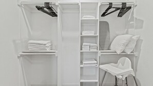 Een witte kast met planken voor opgevouwen handdoeken, een kledingroede en een stoel.
