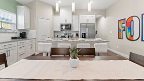 A modern kitchen with white cabinets, a central island, and a dining area with a table and chairs.