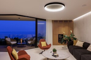 A modern living room with a round coffee table, a sofa, and a chair. There is a large window with a view of the city. - Modern Villa in Dubrovnik with Infinity Rooftop Pool (Dubrovnik)