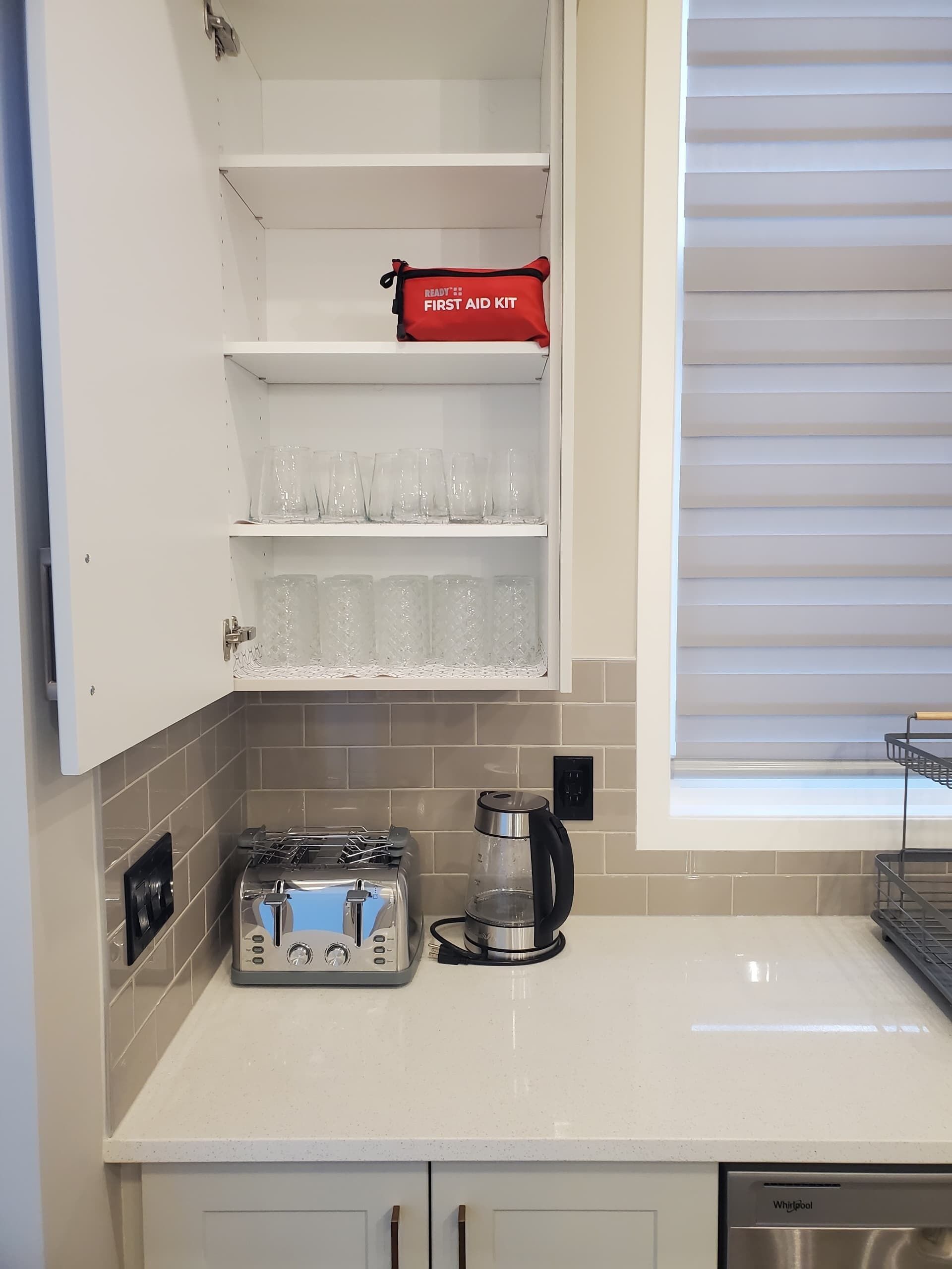 Een keuken met een broodrooster, een koffiezetapparaat en een verbanddoos op een plank.