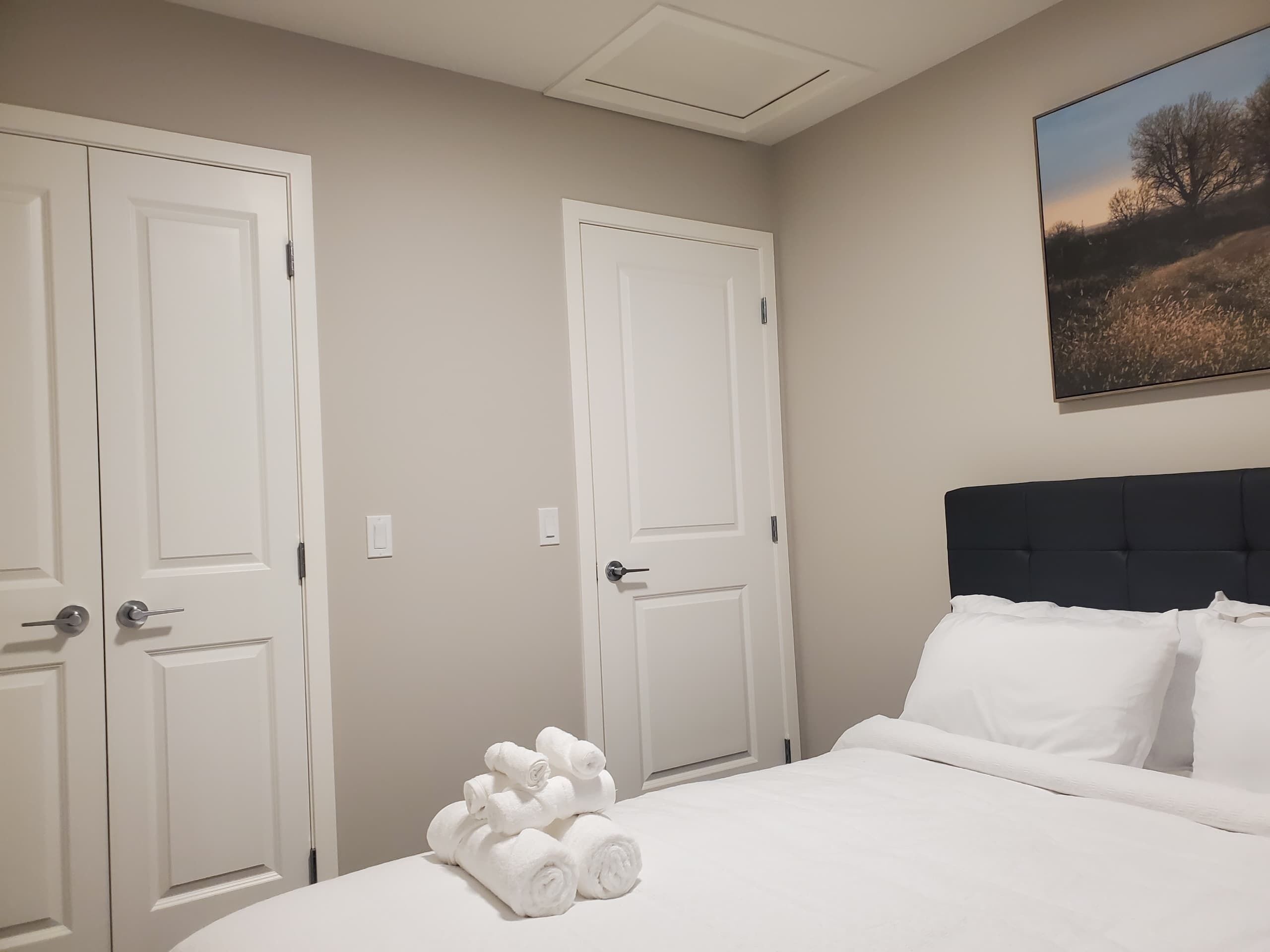 Une chambre d’hôtel avec un lit, deux portes blanches et un tableau au mur.