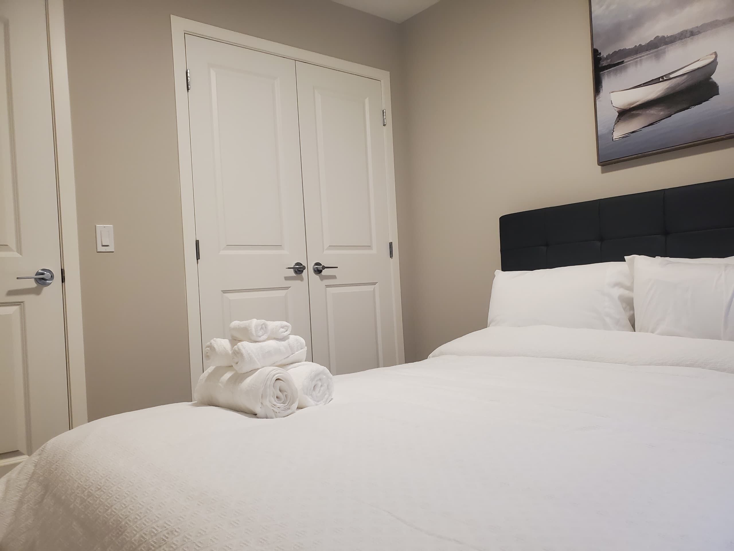A neatly made bed with white linens, a black headboard, and a painting of a boat on the wall.