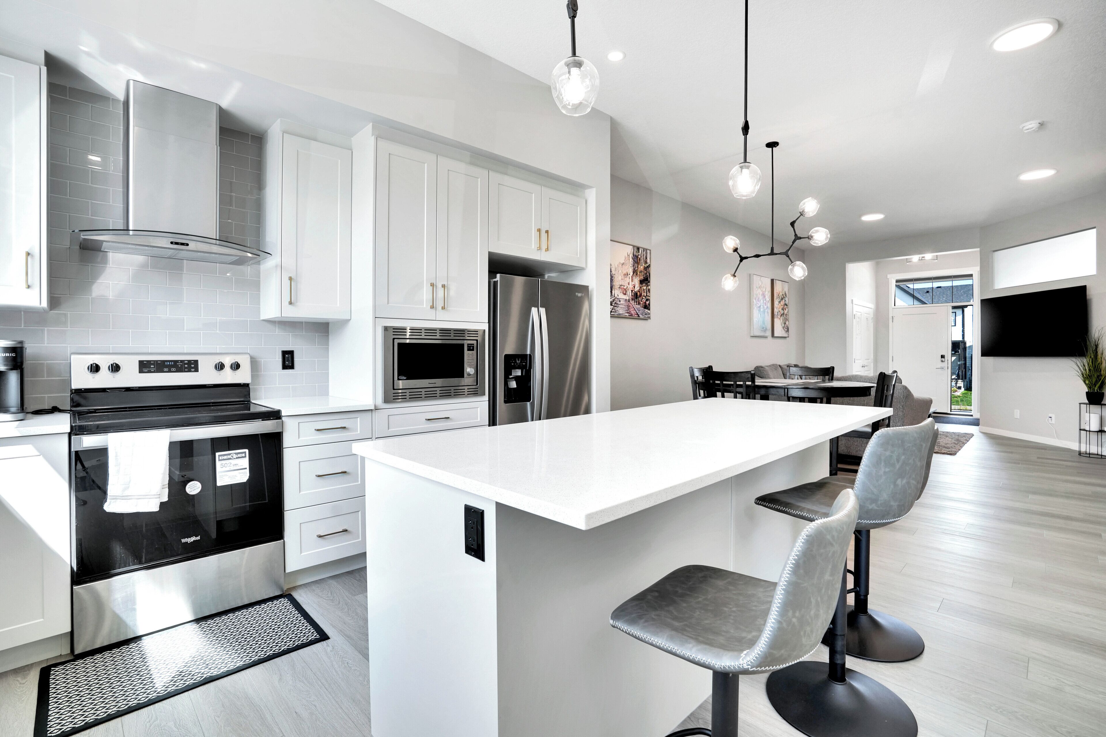A modern kitchen with white cabinetry, stainless steel appliances, and a central island with bar stools.