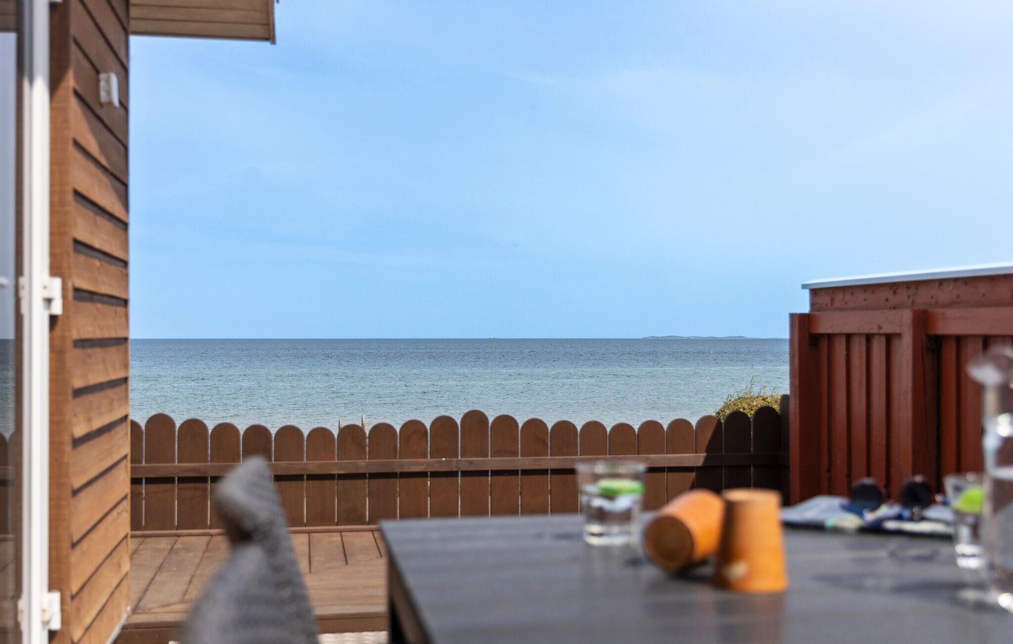 Een houten terras met uitzicht op zee, een hek en een tafel met spullen erop.