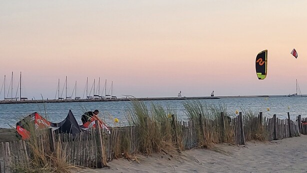 A beach with a wooden fence, a sandy shore, and sailboats in the distance. - La Frégate Town Centre and Beach (Le Grau-du-Roi)