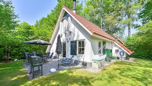 Een huis met een schuin dak, een terras met tuinmeubilair en een schoorsteen.