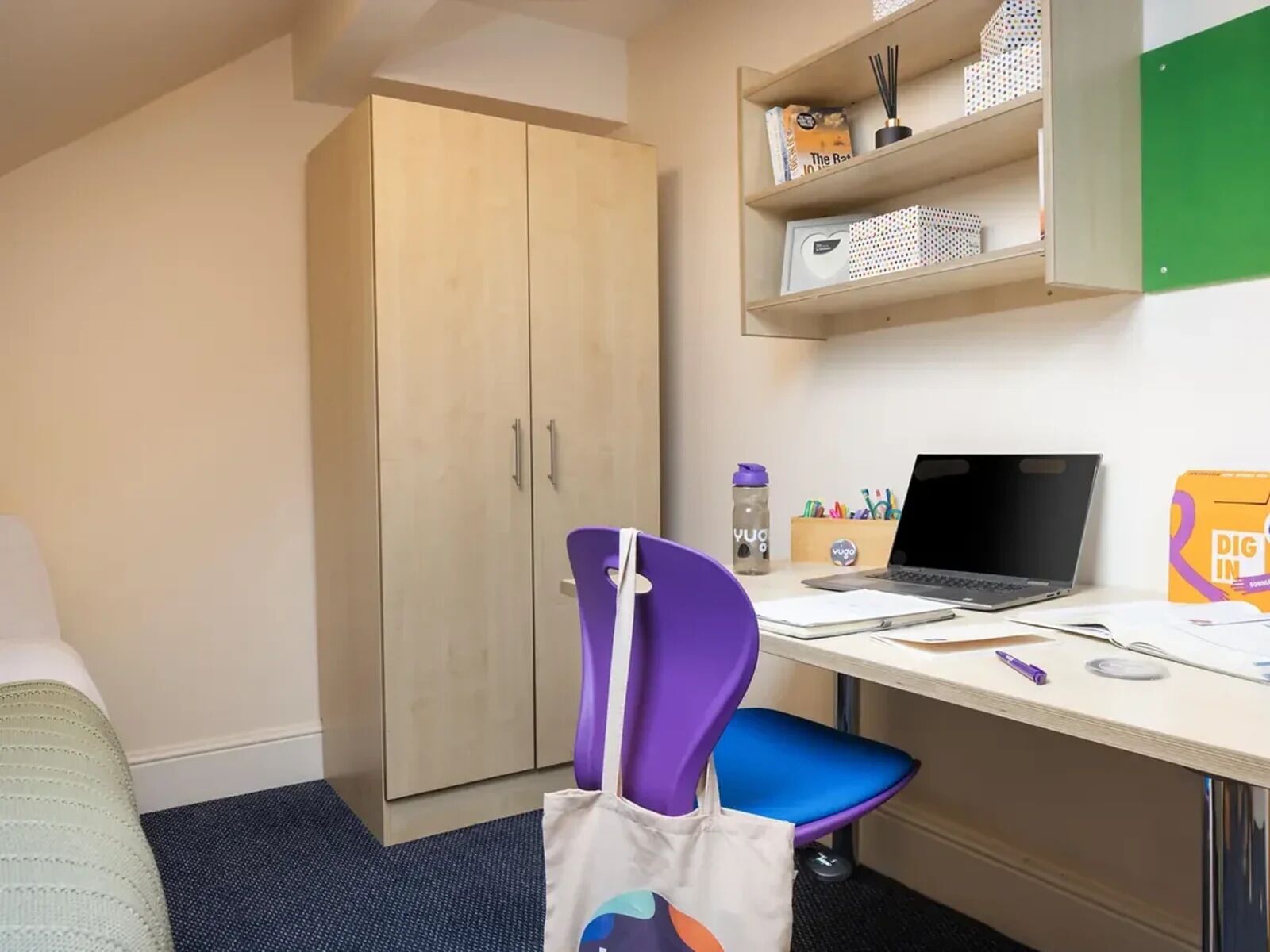 A small office space with a desk, a laptop, a purple chair, a blue chair, a cabinet, and a wardrobe.
