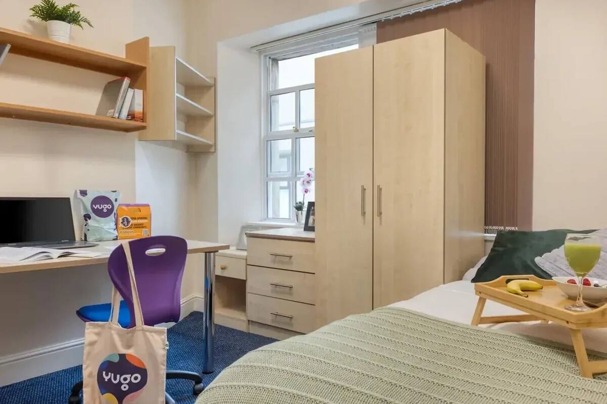 Une chambre d’hôtel comprenant un lit, un bureau avec un ordinateur, une chaise, une armoire et une fenêtre donnant sur un paysage agréable.