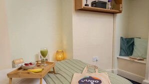 A neatly arranged room with a bed, a tray with breakfast items, a bottle of water, a lamp, and a wall-mounted shelf with a book and a pillow. - Student Only Cable Street (Lancaster)