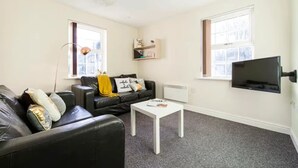 A living room with a black leather sofa, a white coffee table, and a mounted TV. - Student Only Cable Street (Lancaster)