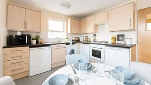 A modern kitchen with light wood cabinets, a dishwasher, a washing machine, and a dining area with a table set for two. - Student Only Cable Street (Lancaster)