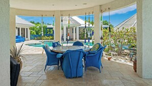 Eine überdachte Terrasse mit Pool, blauem Korbmöbel und Blick auf den Poolbereich.