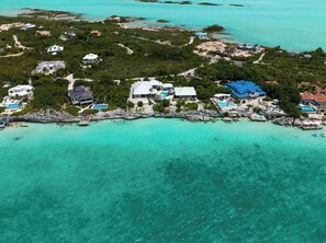 Vista aérea de una propiedad costera con varias casas, aguas turquesas cristalinas y un litoral rocoso.
