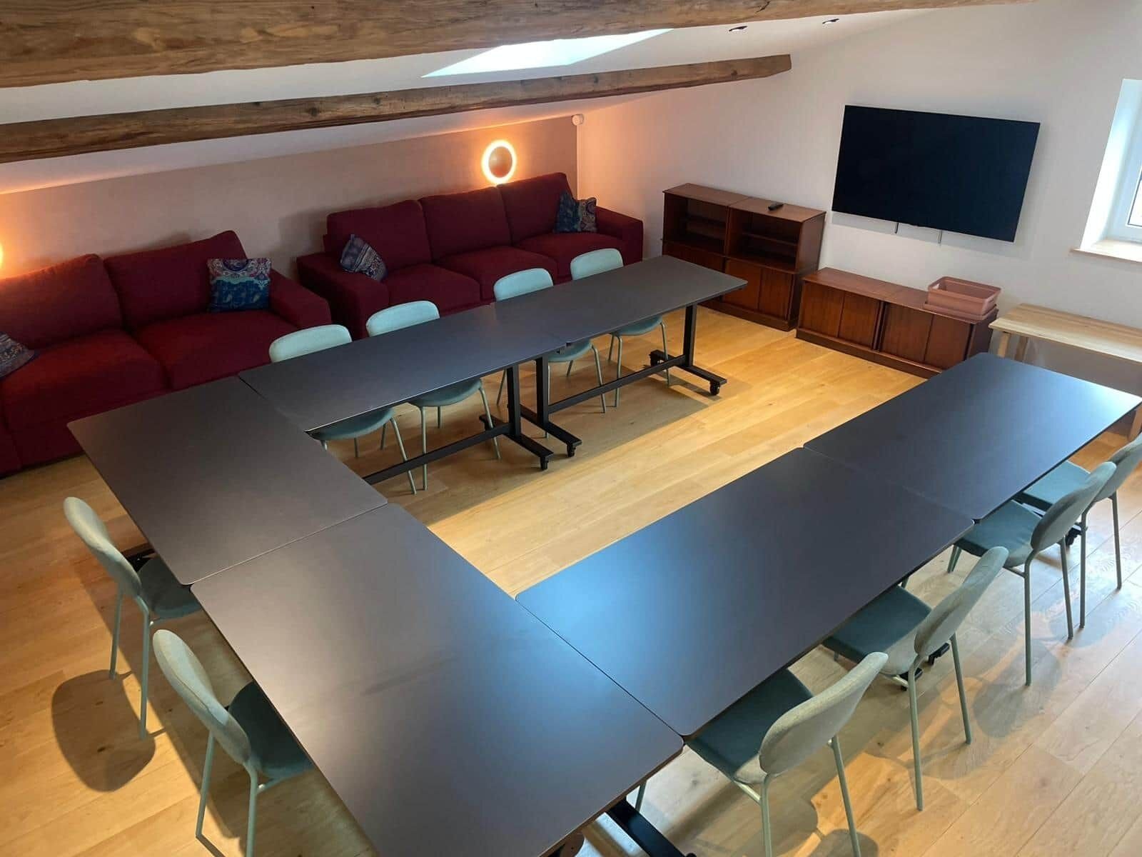 Una habitación moderna con una mesa larga, un sofá rojo y un televisor en la pared.