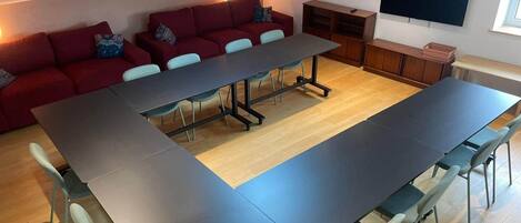 Una habitación moderna con una mesa larga, un sofá rojo y un televisor en la pared.