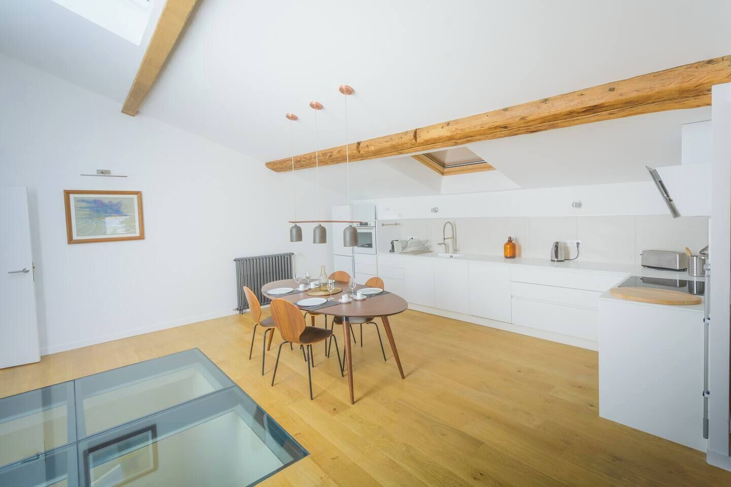 Une cuisine moderne avec des meubles blancs, un plafond en bois et un coin repas doté d’une table en verre.