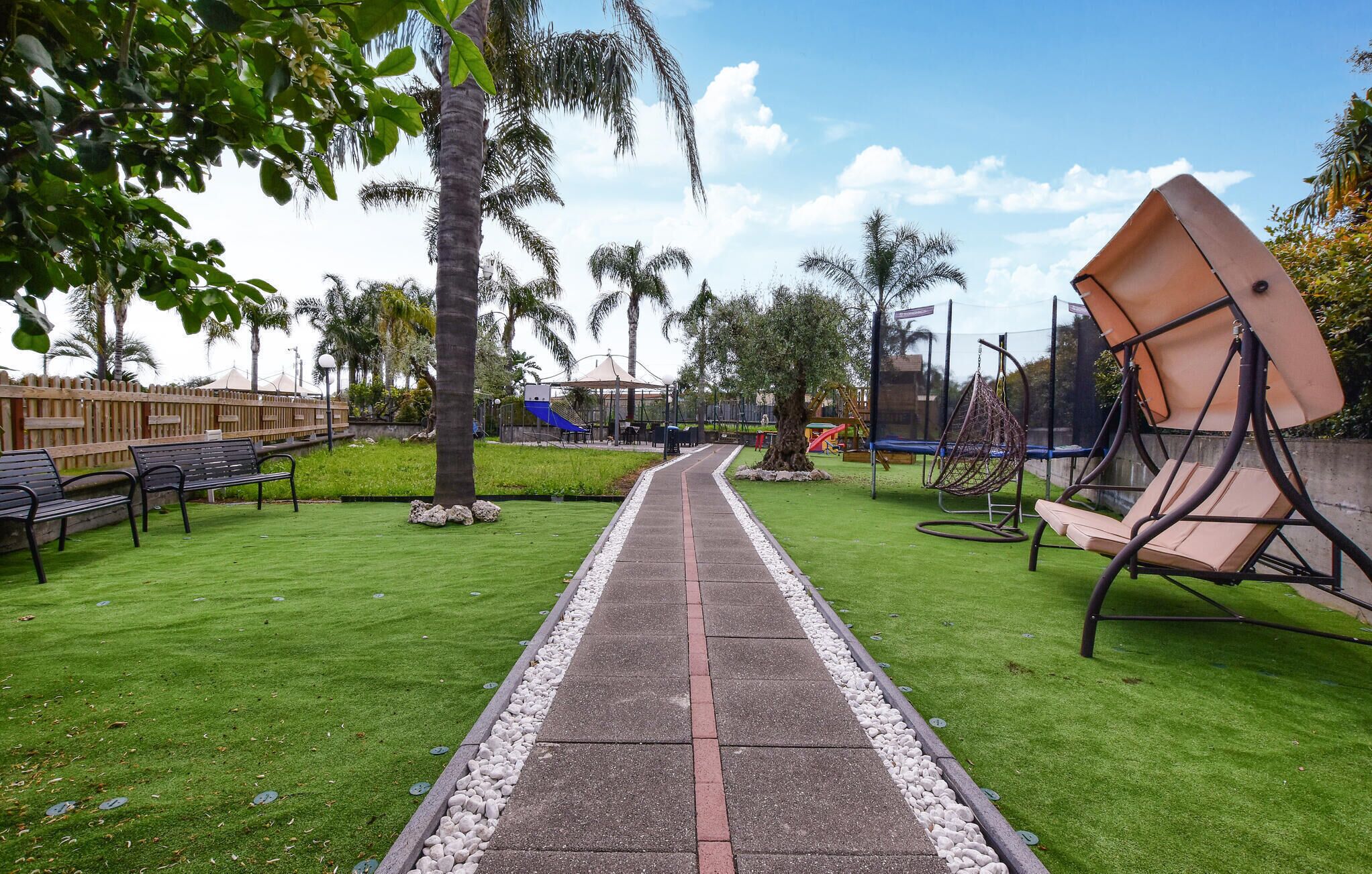 A pathway leading through a park with benches, a swing set, and a playground.