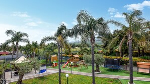 Un'area giochi con scivoli, altalene e una struttura per arrampicarsi, circondata da palme e vegetazione.