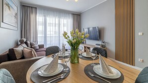 Ein modernes Wohnzimmer mit Essbereich, einer Couch, einem Fernseher und einer Wandpaneele aus Holz.