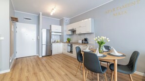 Eine moderne Küche mit weißen Schränken, einem Edelstahlkühlschrank und einem Essbereich mit einem Holztisch und Stühlen.