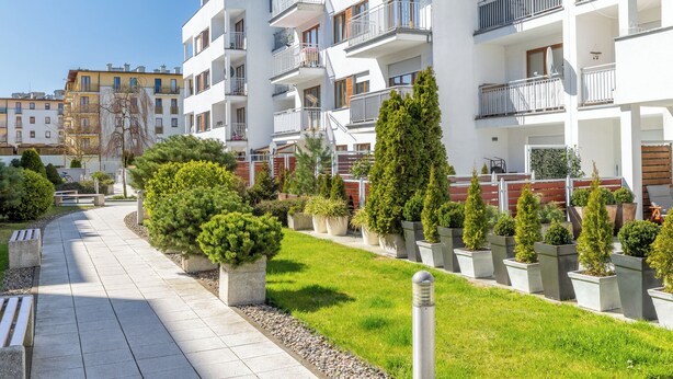Ein modernes Mehrfamilienhaus mit mehreren Balkonen, einem gepflasterten Weg und gepflegter Bepflanzung.