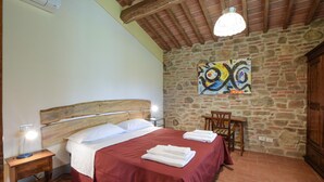 A bedroom with a stone wall, a wooden bed, a red bedspread, a painting, a wooden chair, and a nightstand with a lamp. - Stunning home in Lucignano (Lucignano)