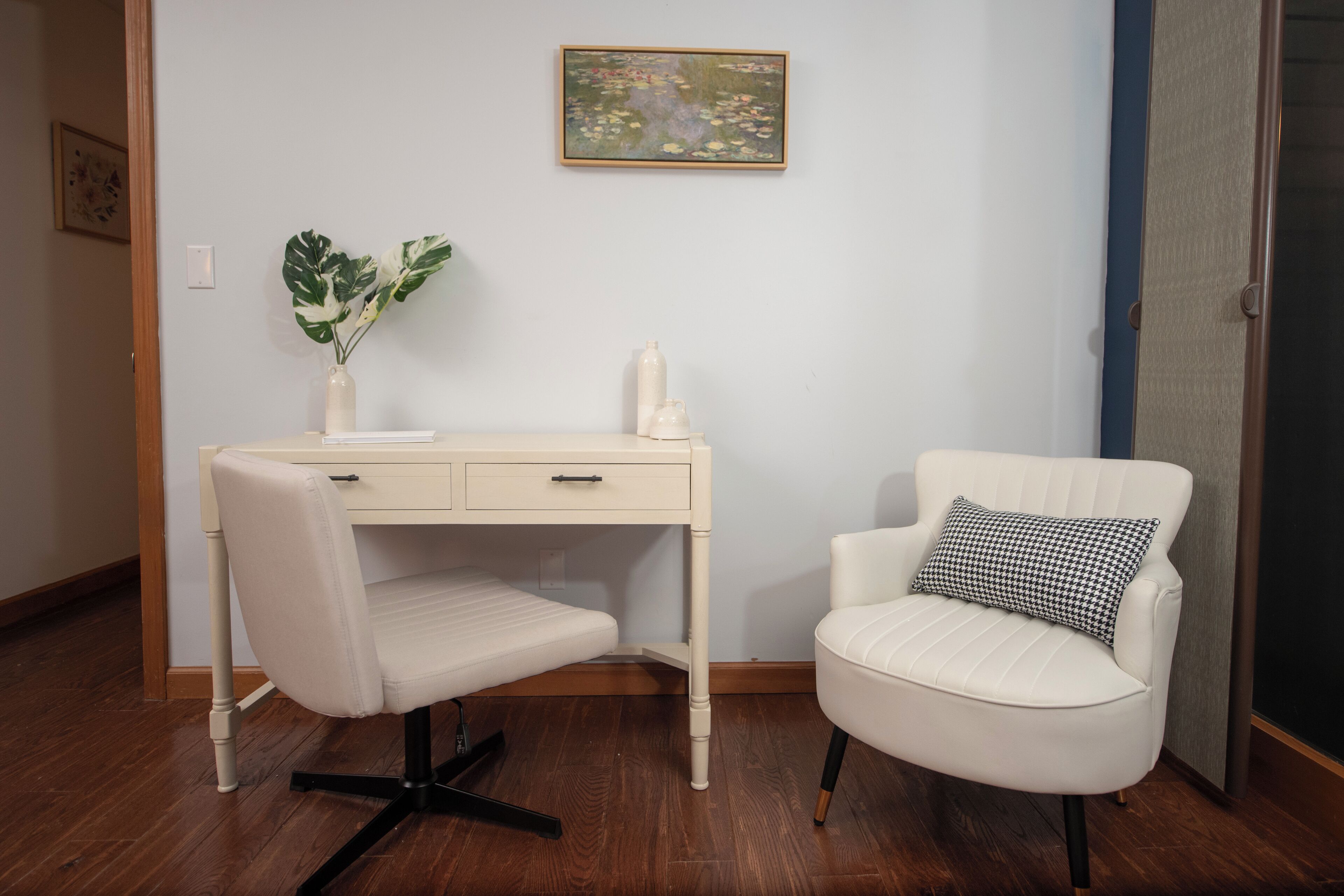 A room with a white desk, a white chair with a patterned pillow, and a plant on the desk.