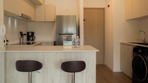 Una cocina moderna con una isla central, dos taburetes de bar, un refrigerador de acero inoxidable, una cafetera y una lavadora.