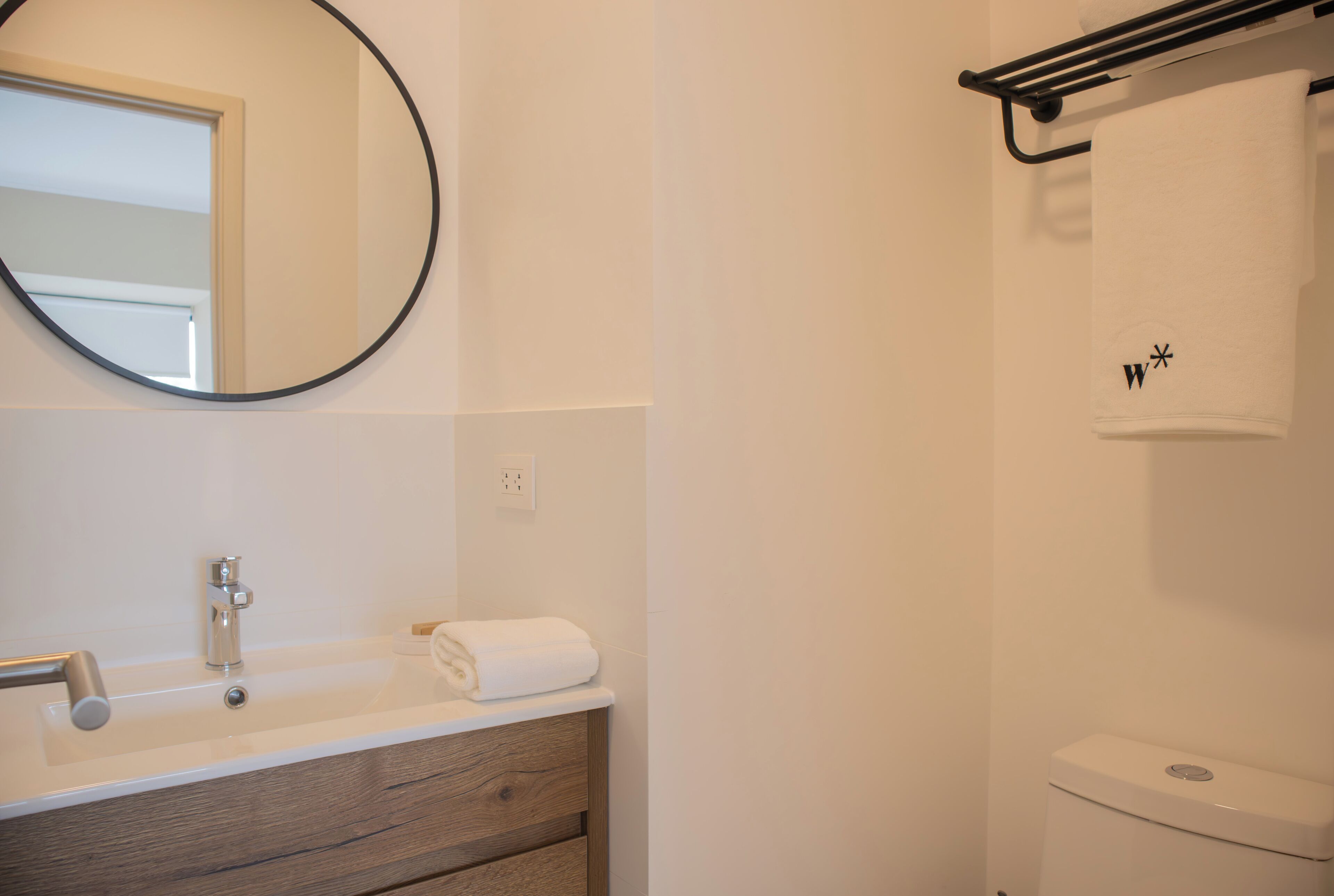 A bathroom with a round mirror, a sink, a towel, and a toilet.