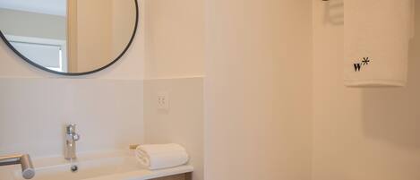 A bathroom with a round mirror, a sink, a towel, and a toilet.