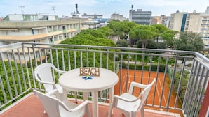 A balcony with a table and chairs, a sign reading "BEACH", and a view of a tennis court and surrounding buildings.