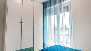 A bedroom with a bed, a wardrobe, and a window with sheer curtains.