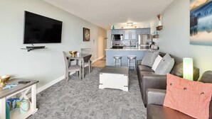 A modern living room with a TV, dining area, and kitchen. - Remodeled Oceanfront Suite - Indoor Pool and Ocean Views! (Lincoln City)