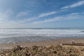 A beach with waves, sand, and sparse vegetation. - Remodeled Oceanfront Suite - Indoor Pool and Ocean Views! (Lincoln City)