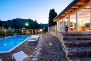 A pool with lounge chairs, a stone patio, and a building with large windows.
